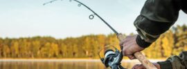 An outdoor fisherman on a lake with the treeline in the background holding a fishing rod as it bends from a catch.