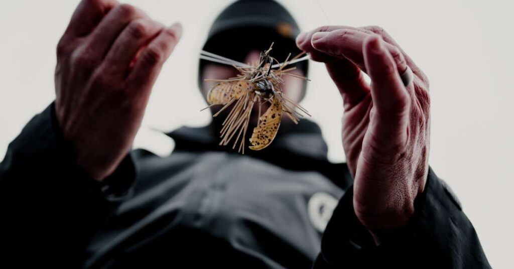 A low point-of-view of a male bass angler tying a fishing lure with the lure and his hands in focus and face blurred.