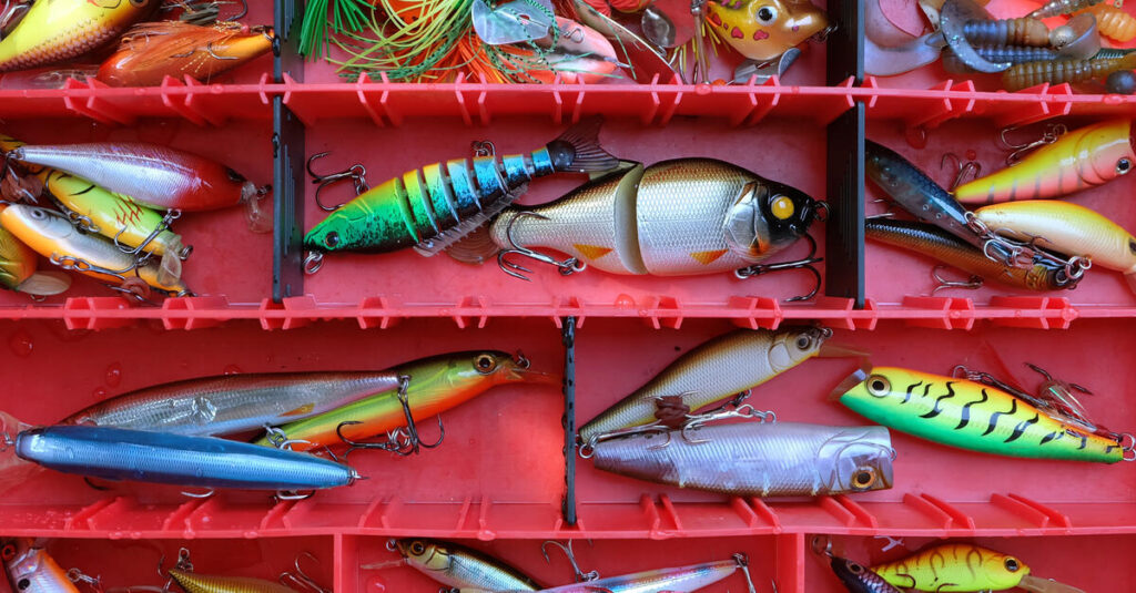 Close-up of multi-colored fishing lures inside a red tackle box. The lures also vary in terms of size.