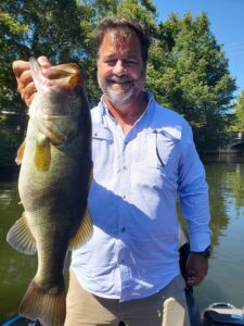 Angler holding a largemouth bass caught at Lake Austin in October 2025 using a Bass Pro Shops Speed Shad paddle-tail swimbait over submerged vegetation in clear water conditions.