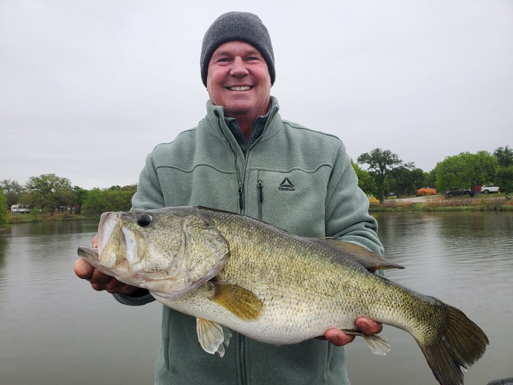 Angler holding a largemouth bass caught on a drop-shot rig during a cold front in a spawning area at Inks Lake