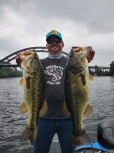 angler holding two largemouth bass caught on a drop shot rig on a shallow grass flat at Lake Austin