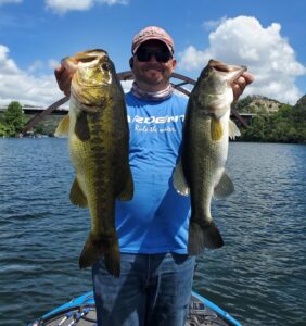 Bassquatch Fishing guide holding two largemouth bass caught on Lake Austin using Neko-rigged creature baits around shallow submerged vegetation.