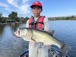 Young angler holding a giant largemouth bass caught on a guided fishing trip at Inks Lake, with the dam in the background
